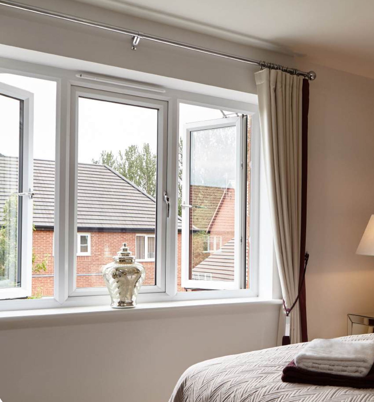 Bedroom with white casement windows, one opened to the garden, cream curtains and a vase on the sill